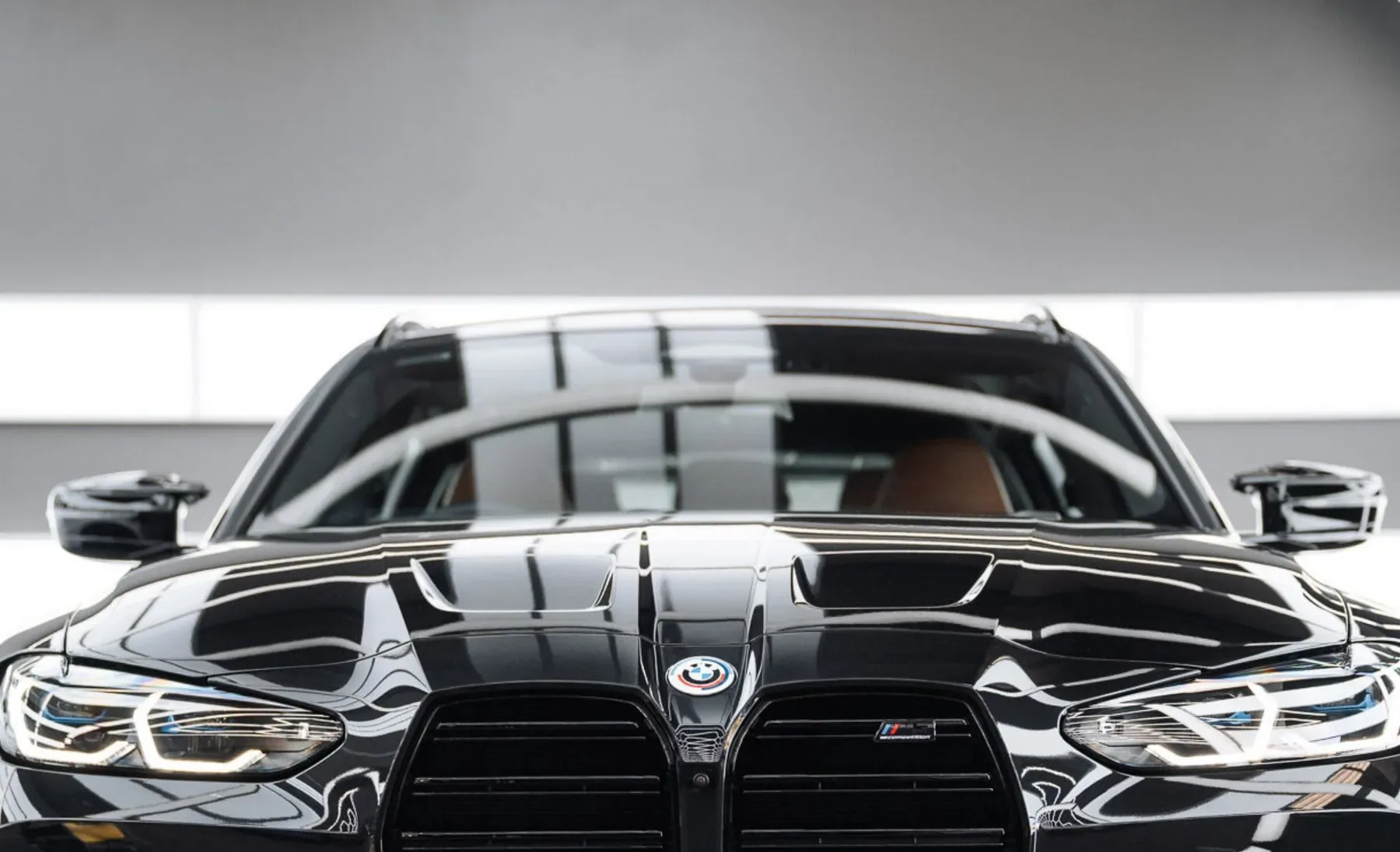 Front of a gloss black BMW M3 with crisp reflections across the bonnet