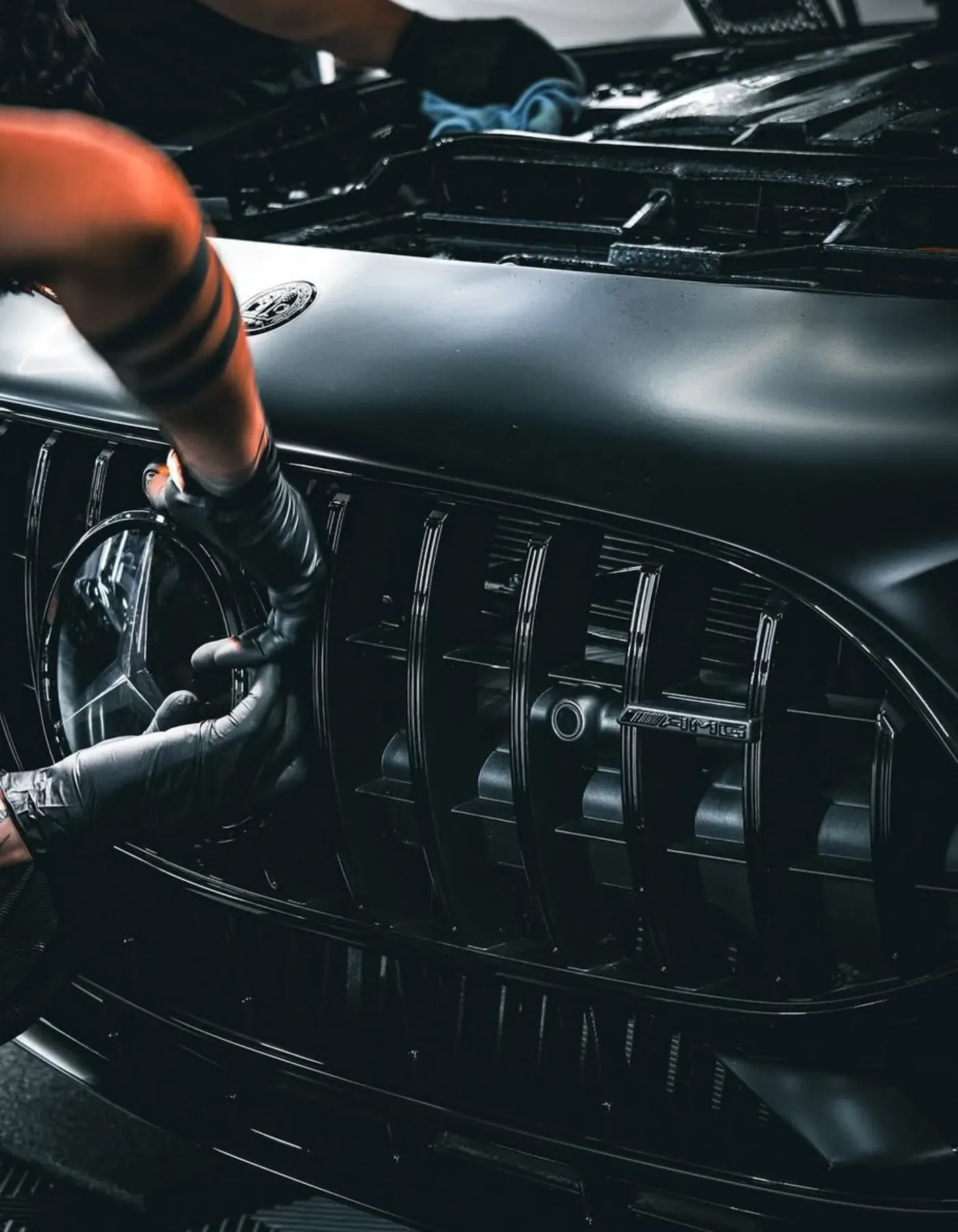 Gloved hands cleaning the grille of a black Mercedes-AMG