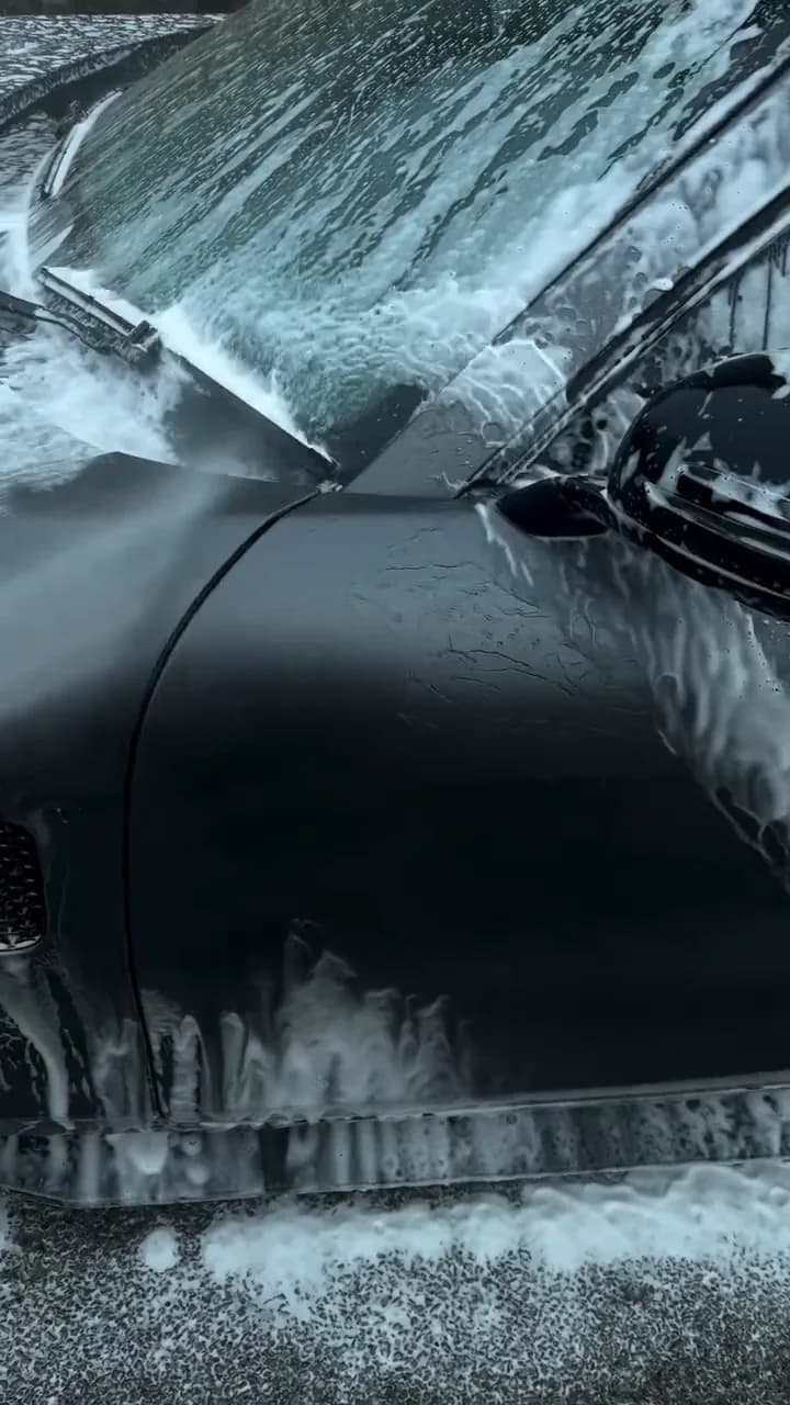 Snow foam being rinsed off a dark car