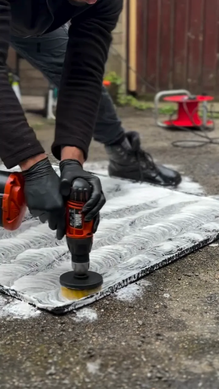 Floor mat being scrubbed and rinsed on a driveway